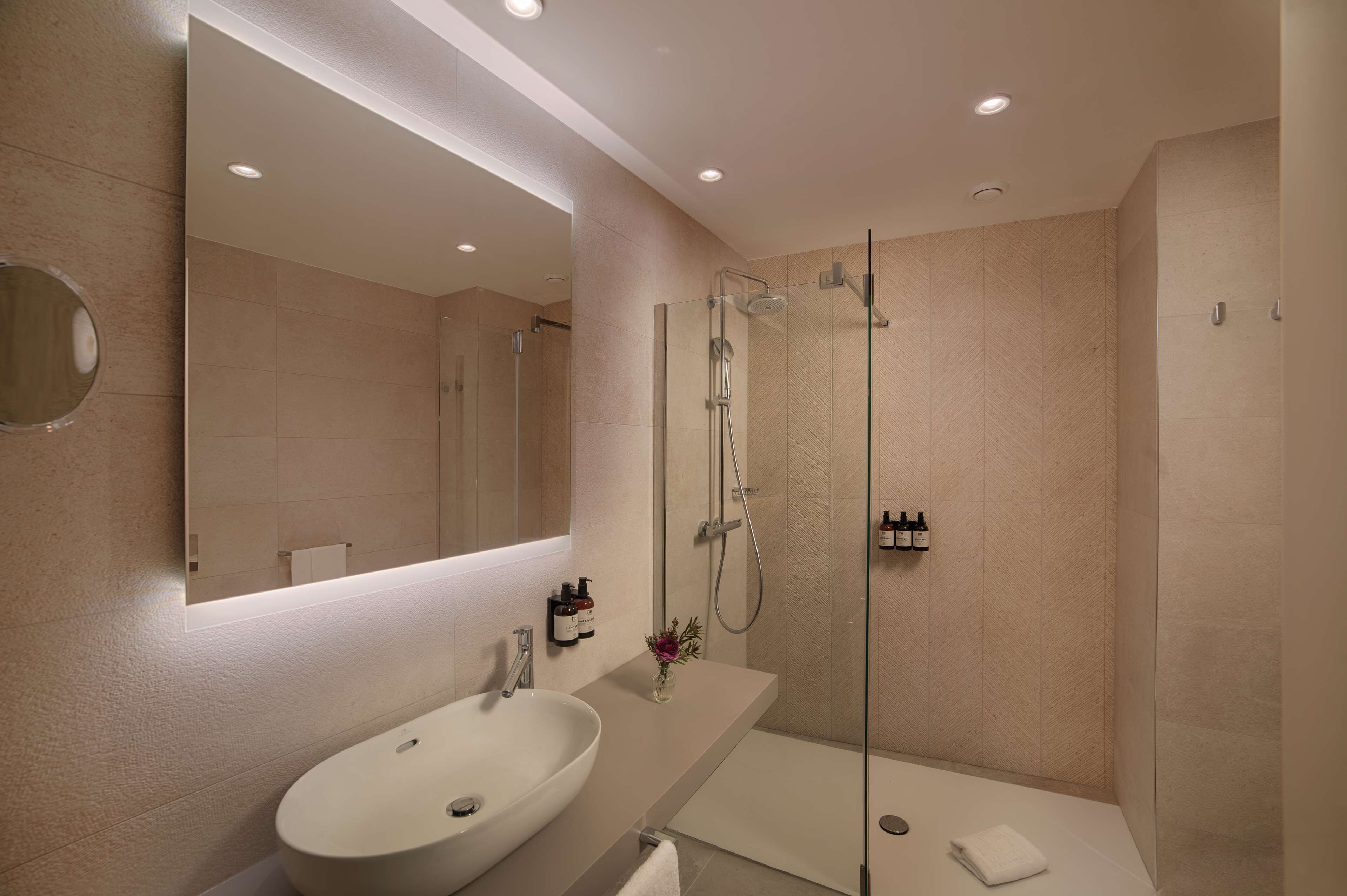 A modern bathroom with a large mirror, a sink, a shower, and a glass-enclosed shower area.
