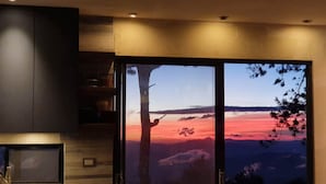 Et værelse med en stor skydedør, der giver udsigt til en smuk solnedgang over bjergene.