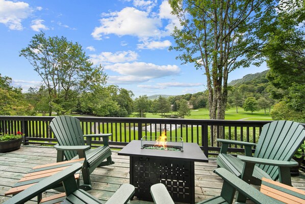 Une terrasse dotée de chaises Adirondack, d’un foyer extérieur et offrant une vue sur un terrain de golf.
