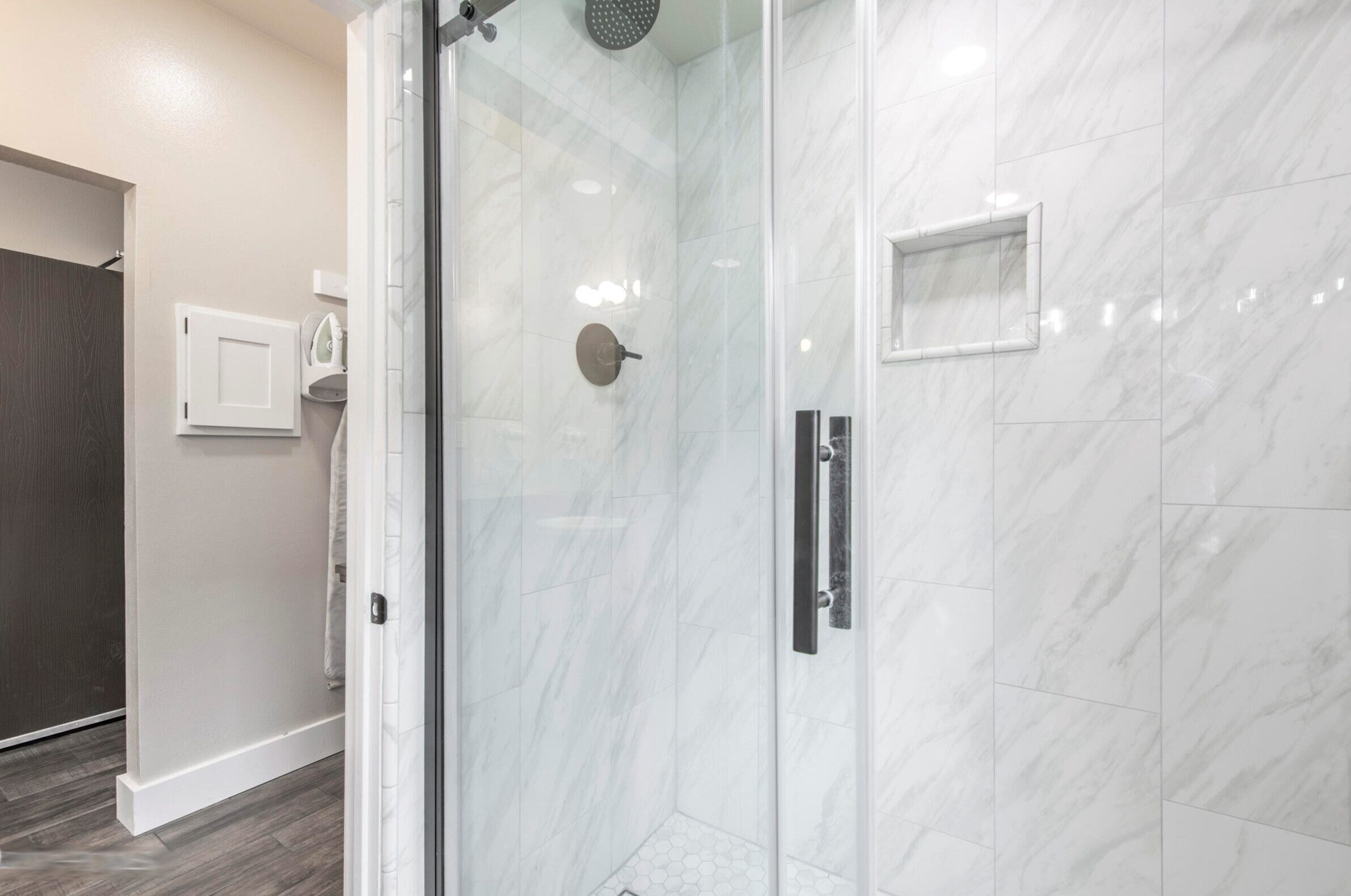 A modern bathroom with a glass shower enclosure, marble tiles, and a dark wood floor.