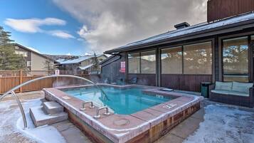 Een hottub met een metalen reling, omringd door een houten terras en een overdekte zithoek.