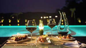 A dining table with plates of food and wine glasses, set against a poolside view at night. - Rosetta-Sakleshpur (Alur)