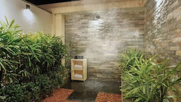 Un área de spa con pared de piedra, un banco de madera con toallas y plantas verdes.