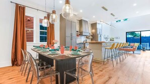 Et moderne køkken med en central ø, rustfrie hvidevarer og et spiseområde med et rundt bord og stole.