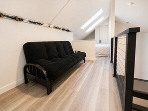 Quarto de estilo loft moderno com sofá preto, piso de madeira, porta branca e claraboia.