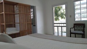 Een slaapkamer met een bed, een houten garderobe, een stoel en een raam met uitzicht op groen.