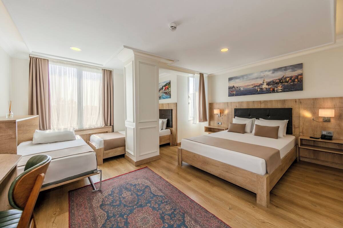 A hotel room with a bed, a desk, a chair, a nightstand, and a painting on the wall.