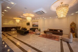 A spacious lobby with a reception desk, multiple seating areas, chandeliers, and a large clock. - Porta Romanos Hotel (Istanbul)