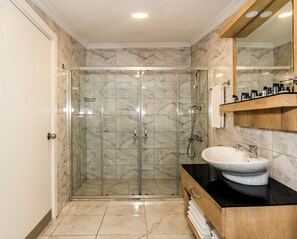 A modern bathroom with a glass-enclosed shower, a white sink, and a wooden vanity. - Porta Romanos Hotel (Istanbul)