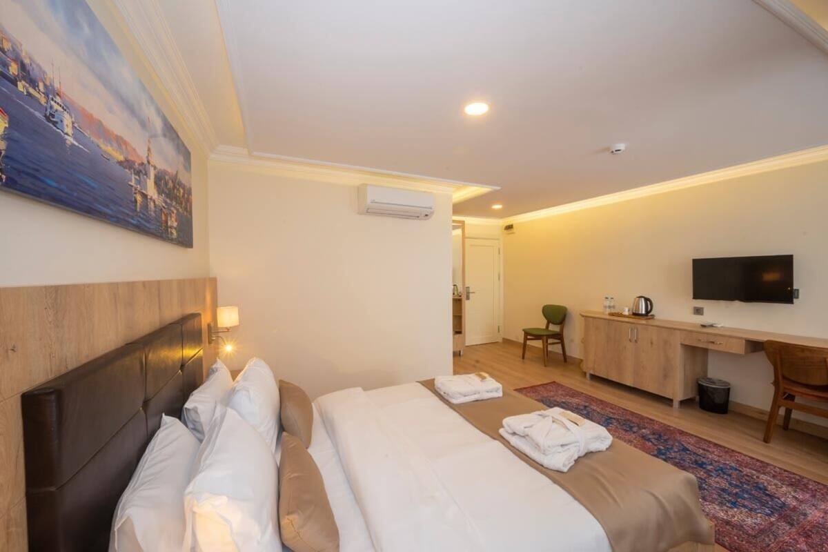 A hotel room with a bed, a desk, a chair, a television, and a painting on the wall.