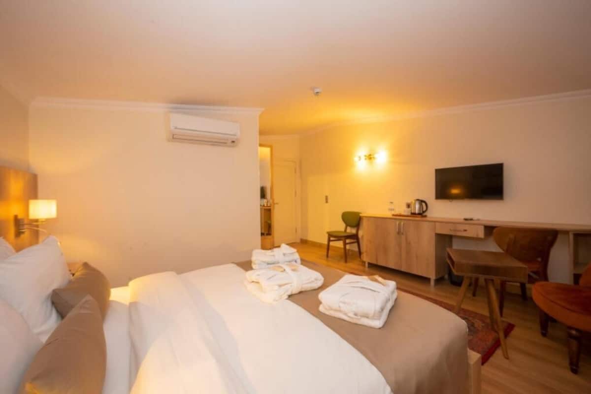 A hotel room with a bed, a desk, a chair, a television, and a bathroom visible in the background.