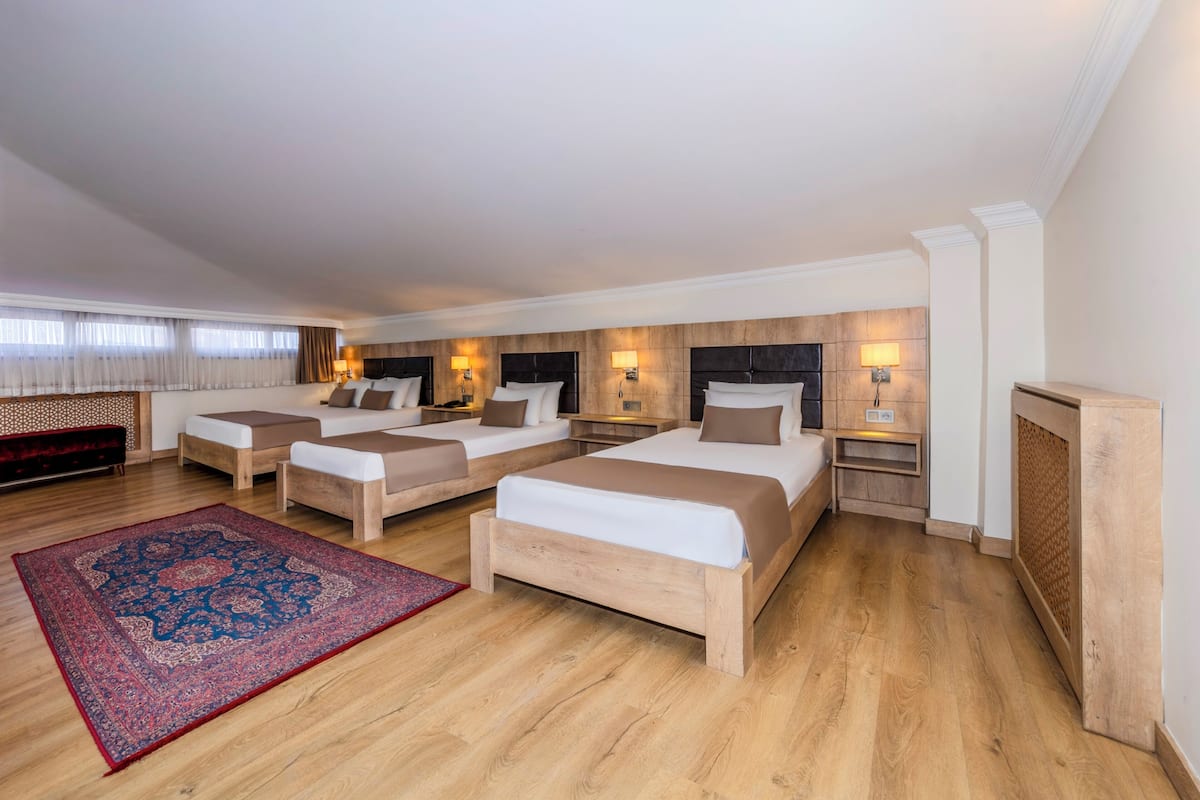 A hotel room with three beds, wooden headboards, and a large red and blue rug.