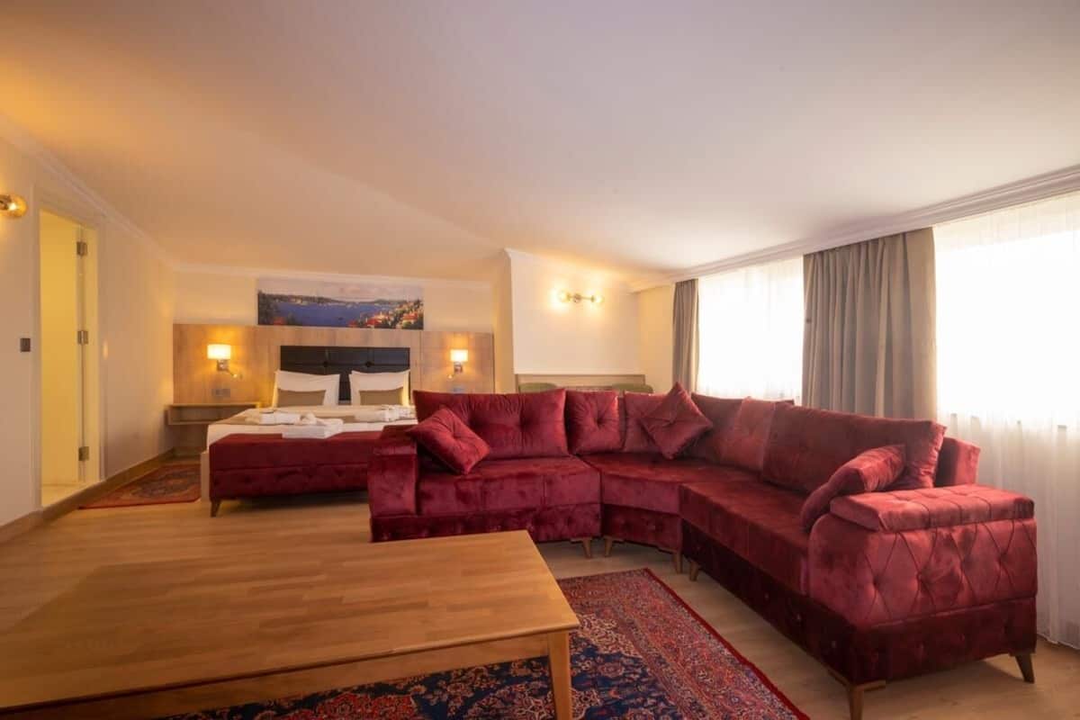 A hotel room with a large red velvet sofa, a wooden coffee table, and a bed with white linens.