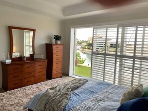 A bedroom with a bed, dresser, mirror, and a view through large windows.