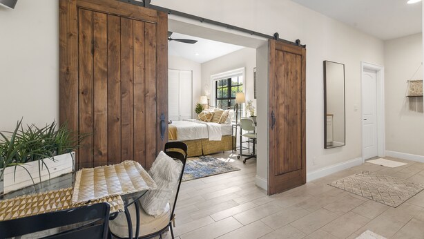A room with a bed, a desk, and a chair. There is a sliding door and a mirror on the wall.