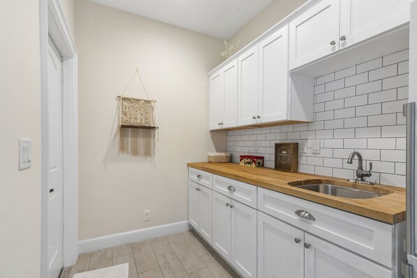 A kitchen with white cabinets, a wooden countertop, and a tiled backsplash.