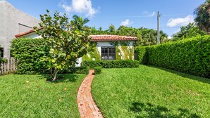 A small house with a red-tiled roof, a brick pathway, and lush green hedges.