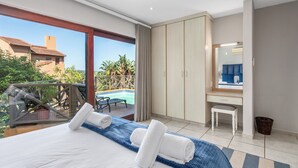 A hotel room with a bed, a desk, a chair, a large window, and a view of an outdoor swimming pool. - San Lameer Villa Rentals 14201 (Southbroom)