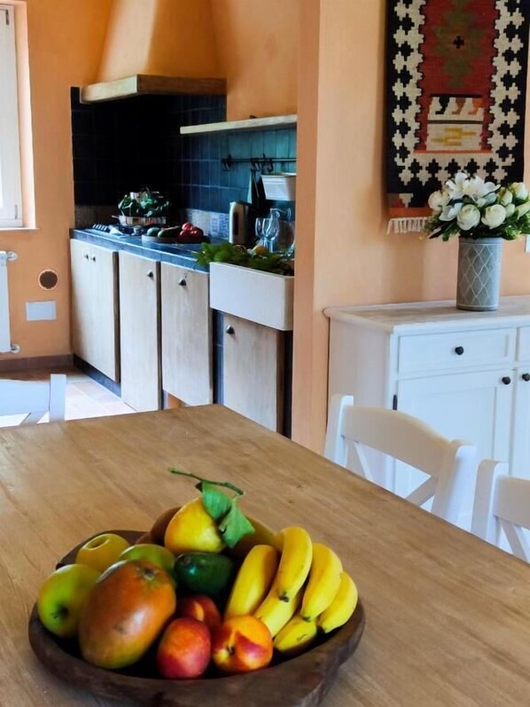 A kitchen with cabinets, a countertop, and a dining table with a fruit bowl.