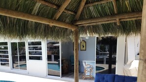 A covered outdoor seating area with a pool, wicker furniture, and a thatched roof. - Blissful, serene waterfront Deerfield Beach retreat. Close to the beach. (Deerfield Beach)