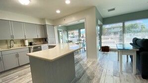 A modern kitchen with a central island, a dining area with a glass table, and a living room with a sofa. - Blissful, serene waterfront Deerfield Beach retreat. Close to the beach. (Deerfield Beach)