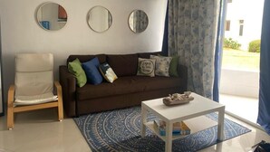 A living room with a brown sofa, a white armchair, a coffee table, and three wall mirrors. - Cómodo y Confortable Estudio Frente al mar (Playa Juan Dolio)