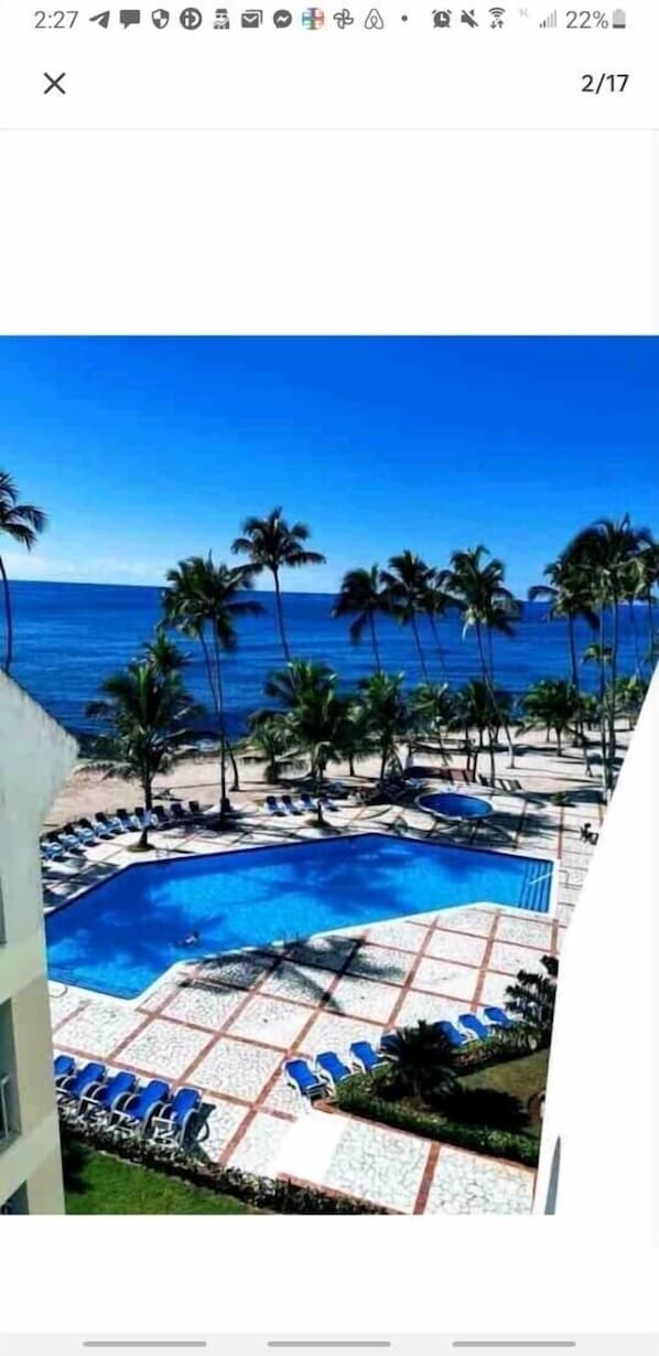 A pool area with a clear view of the ocean, surrounded by palm trees and lounge chairs.