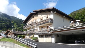 Un hotel de varios pisos con balcones, un estacionamiento y montañas al fondo.