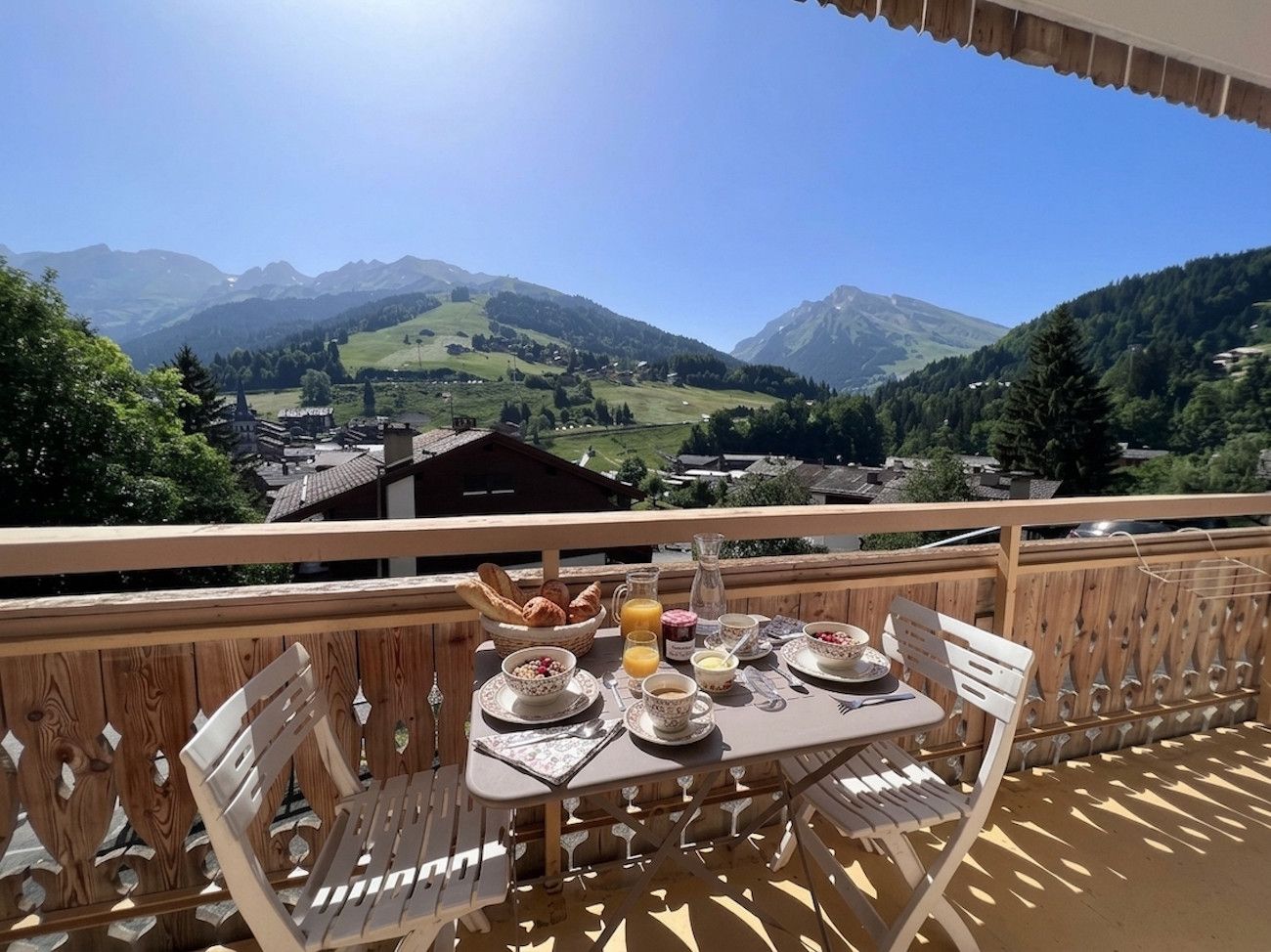 A wooden deck with a table set for breakfast, overlooking a mountainous landscape.