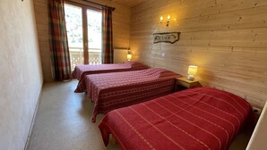 Una habitación con dos camas, paredes de madera, una ventana con cortinas y una lámpara fijada a la pared.