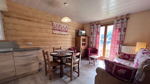 Habitació d'estil cabana acollidora amb interior de fusta, taula de dinar amb cadires, butaca vermella, sofà petit i televisió damunt un moble de fusta.