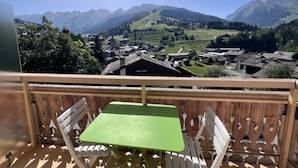 A balcony with a green table and white chairs, overlooking a village with mountains in the background. - CREPUSCULE 5 - Apartment near ski slopes and village - Wi-Fi - Parking (La Clusaz)