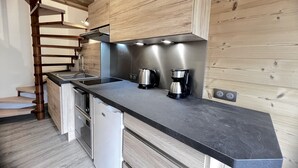 A modern kitchen with wooden cabinetry, a black countertop, stainless steel appliances, and a built-in stove. - CREPUSCULE 5 - Apartment near ski slopes and village - Wi-Fi - Parking (La Clusaz)