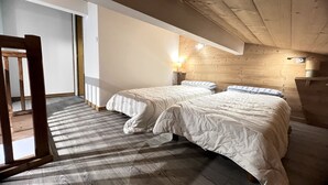 A bedroom with two beds, wooden ceiling beams, a nightstand with a lamp, and a window allowing natural light. - CREPUSCULE 5 - Apartment near ski slopes and village - Wi-Fi - Parking (La Clusaz)