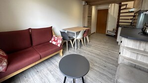 A cozy living area with a red sofa, a small round table, and a wooden dining table with chairs. - CREPUSCULE 5 - Apartment near ski slopes and village - Wi-Fi - Parking (La Clusaz)