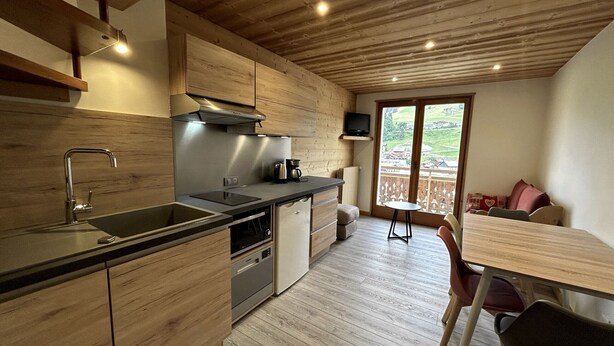 A modern kitchen with wooden cabinets, a sink, and a stove. There is a dining area with a table and chairs. - CREPUSCULE 5 - Apartment near ski slopes and village - Wi-Fi - Parking (La Clusaz)