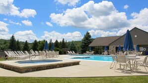 A pool area with lounge chairs and umbrellas, a stone border, and a building in the background. - Prime Resort Location, Modern Ski/Out w/ Balcony (Champion)