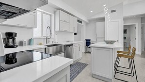 A modern kitchen with white cabinetry, a central island, and a bar area with stools. - Luxury & Comfy Pool Getaway ~ Mins to Beaches & DT (Fort Lauderdale)