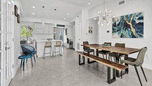 A modern kitchen with white cabinets, a dining area with a wooden table and benches, and a large abstract painting on the wall. - Luxury & Comfy Pool Getaway ~ Mins to Beaches & DT (Fort Lauderdale)