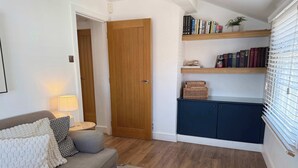 A living room with a sofa, a coffee table with decorative items, a bookshelf with books, a wooden door, and a window with blinds. - Beautiful Cuppin Street Two Bed Apartment (Chester)