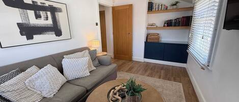 A living room with a grey sofa, a round coffee table with a plant, and a bookshelf with books and decorative items.
