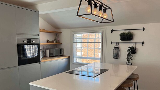 A modern kitchen with grey cabinets, a built-in oven, a microwave, and a large island with bar stools. - Beautiful Cuppin Street Two Bed Apartment (Chester)