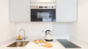 A modern kitchen with a stainless steel sink, a kettle, a cutting board, and a built-in oven. - Snug Cuppin Street Apartment (Chester)