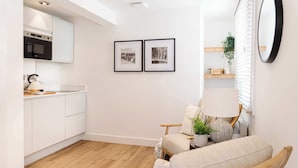 A modern kitchen with white cabinets, a wooden floor, and a dining area with a chair and table. - Snug Cuppin Street Apartment (Chester)