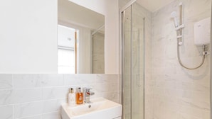 A bathroom with a white sink, a glass shower enclosure, and a white tiled wall. - Snug Cuppin Street Apartment (Chester)