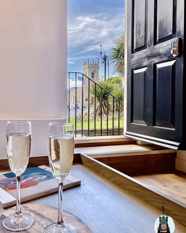 A balcony with two glasses of white wine, a view of a church, and a black door with a phone on it.
