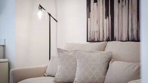 A room with a sofa, two pillows, a floor lamp, and a wall art piece.
