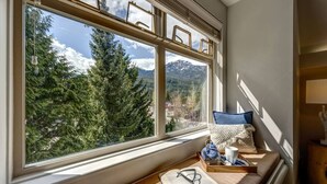 Un rincón acogedor para leer con un ventanal grande que da a un bosque y montañas.