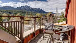 Un balcón con sillones de mimbre y una mesa, con vista a un paisaje montañoso.