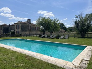 A rectangular swimming pool with clear blue water, surrounded by a stone border. There are lounge chairs aligned along the pool's edge.